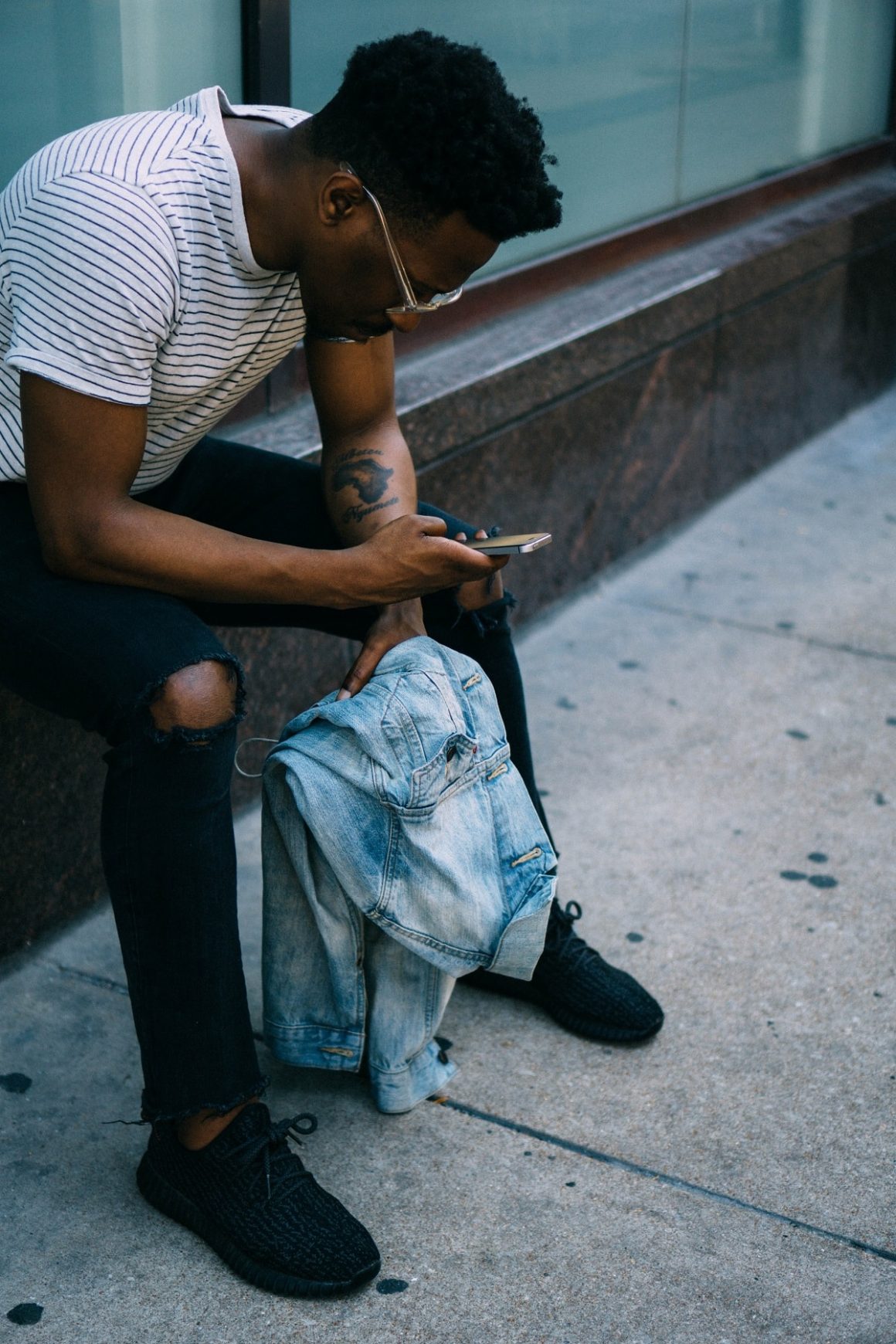 man sitting on the side of a building looking at his phone