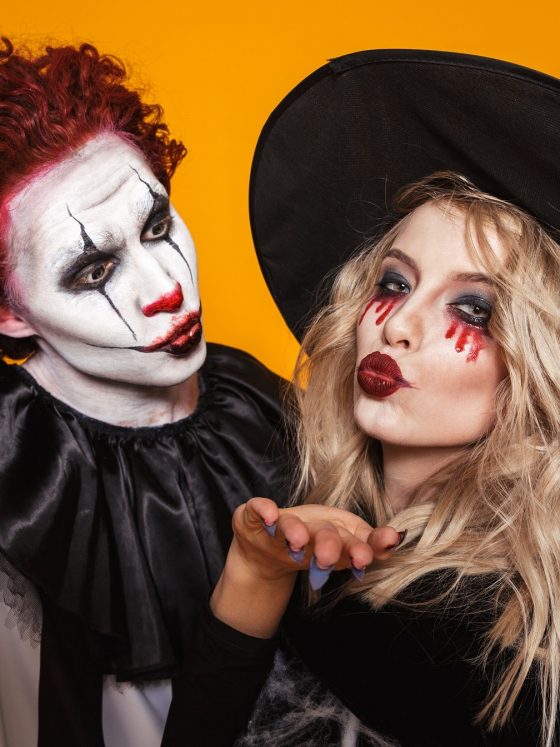 scary clown and wizard in halloween costumes making selfie to camera isolated over orange