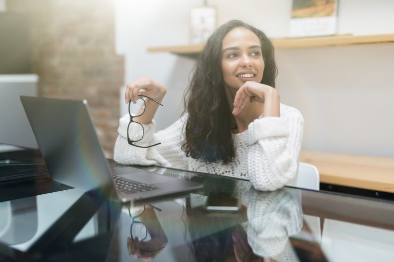 Smiling young woman using laptop thinking about money and finances